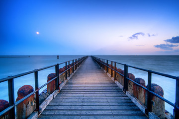 Fototapeta na wymiar Long wooden pier extends over water toward the horizon. A leading line to the horizone