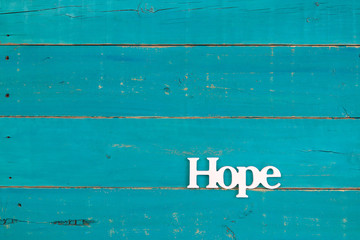 The word Hope hanging on rustic teal blue wood background; religious background with copy space