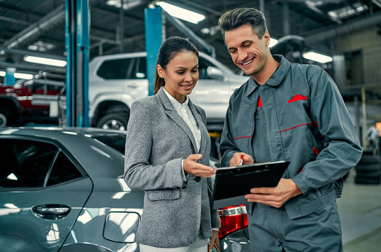 Beautiful businesswoman and auto service mechanic are discussing the work and signing documents. Car repair and maintenance.