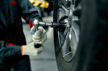 Detail image of mechanic hands with tool, changing tyre of car, with blurred background of garage.