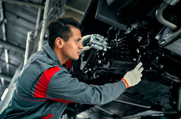 Fototapeta na wymiar Handsome mechanic in uniform is working in auto service. Car repair and maintenance.