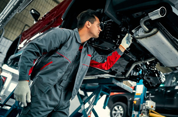 Handsome mechanic in uniform is working in auto service. Car repair and maintenance.