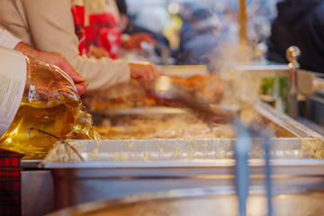 Pouring oil into deep fryer with deep fried Reibekuchen, Kartoffelpuffer, Potato Pancakes on boiling oil in front of stall at Weihnachtsmarkt, Christmas Market, in Düsseldorf, Germany.