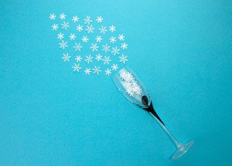 Champagne glass with snowflake shaped confetti on blue background.