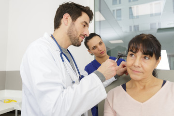 male doctor examining senior female patients ear with otoscope