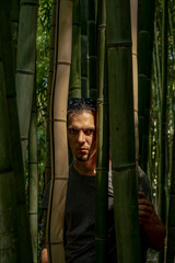A young man with dark hair standing among the bamboo. The sun illuminates the face