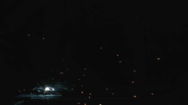 Forge workshop. Smithy. Worker in a welding hood helmet welds a part by electric welding. Sparks are reflected in the protective screen. Blacksmith makes iron product for manufacture. Slow motion.