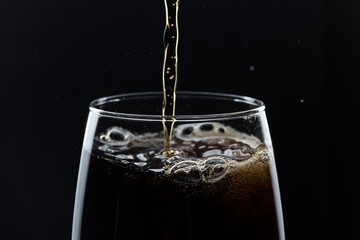Glass of pouring fizzy drink with ice on a black background