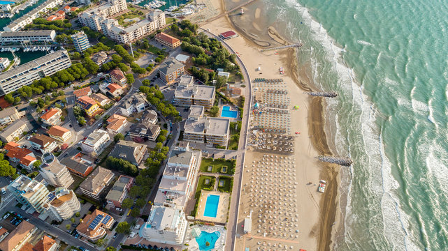 Beautiful beach at sunset with umbrellas and loungers. Adriatic Sea near town of Lignano Sabbiadoro Italy. Sea coastline in Italy, Europe during summer sunny day. Holiday and vacation concept.