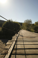 Wooden rope suspension bridge for walk crossing river.