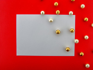 It's holiday time! Festive blank white greeting card on a red background with shiny and glittering ornaments, and a Christmas tree. Top view.