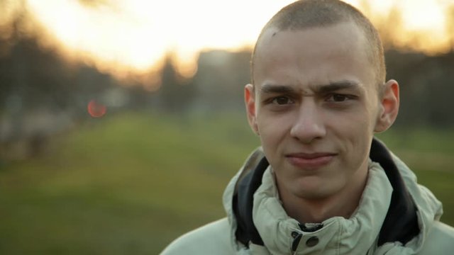 Handsome pensive young man with short hair looking at camera in the park in a chilly evening