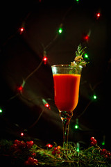 red Christmas glass with drink, cocktail decorated in new year style, green branch, clothespin and berry, on a dark background