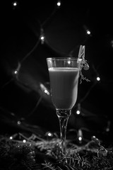 black and white photo new year's glass with drink, cocktail decorated in new year's style, branch, clothespin and berry, on a dark background