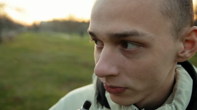 Funny wide angle closeup portrait of smoking e-cigarette young man in the park in the evening