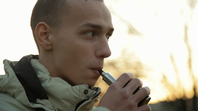 Camera follows hand of vaping boy in the park, close up