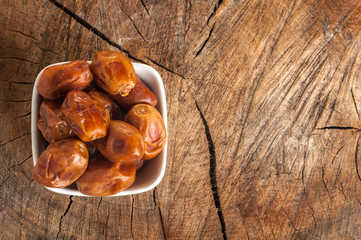 White bowl of dried dates. Tasty date in a white bowl on a wooden aged background. View from above