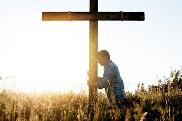 Male with his head leaned against a hand made wooden cross while praying