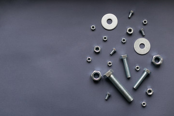 Metallic screws, bolts and gears on the dark grey background