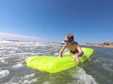 Boy floats on yellow green inflatable mattress near the sandy beach. Adriatic Sea near town of Lignano Sabbiadoro Italy. Kids swim and bathe in water. Summer sunny day.