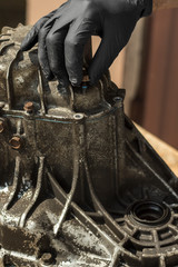 Dłoń mechanika w czarnej nitrylowej rękawiczce ochronnej odkręca śrubę z obudowy skrzyni biegów.