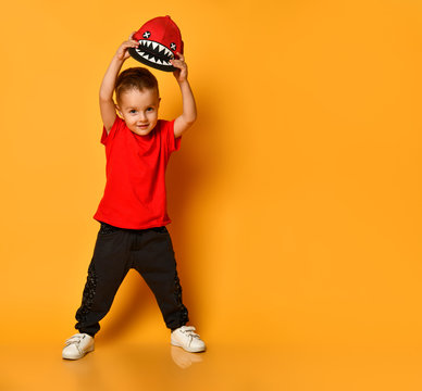 Young guy boy in a red T-shirt and dark pants, white sneakers and a funny cap posing on a free copy space on a yellow background