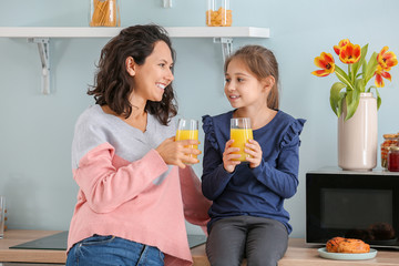 Little girl with her mother drinking juice in kitchen