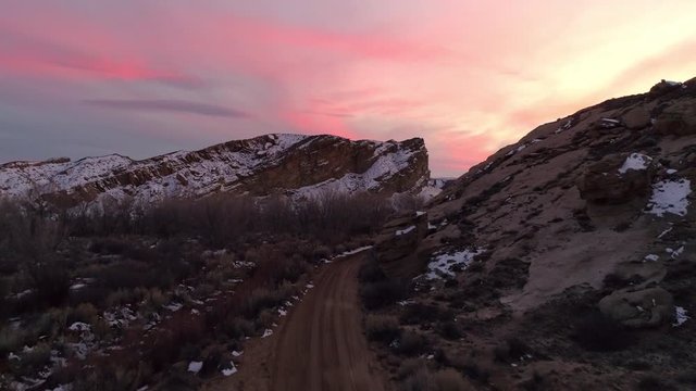 Flying over dirt road and rising above the landscape viewing colorful sunset in the desert during winter in Utah.
