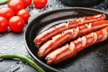 Frying pan with tasty grilled sausages on wooden table