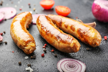 Tasty grilled sausages with vegetables and spices on dark background