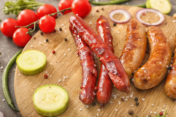 Tasty grilled sausages with vegetables and spices on wooden board