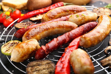 Tasty grilled sausages with vegetables on grid, closeup