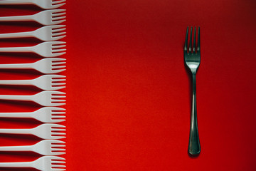 A lot of plastic forks and one metal on a red background.