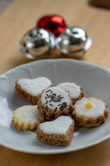 Jam and cream filled cookies with sugar sweet white icing on white plate on wooden table, group of Christmas sweets