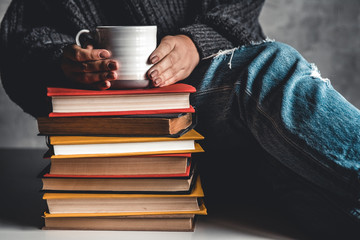 Stack of books with mug on top in front of woman reading book, education, training, hobbies