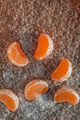 pieces of tangerine in the snow in winter on a wooden background