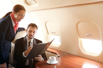 Air hostess showing menu to businessman on board the modern private airplane
