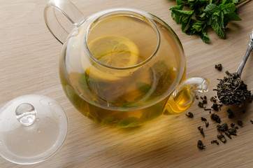 Cup and teapot of herbal tea with fresh mint on wooden