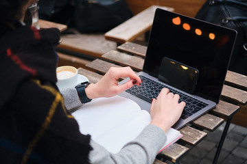 Close up student working on laptop with notepad in cafe on city street