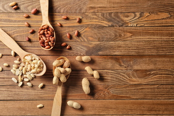 Spoons with peanuts on wooden background