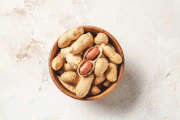 Bowl with peanuts on light background