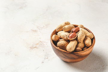 Bowl with peanuts on light background