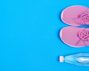 Pink sport shoes and bottle of water on a blue background. Concept healthy lifestyle, sport and diet. Text space. Top view. Flat lay. 