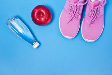 Pink sport shoes with red apple and bottle of water on a blue background. Concept healthy lifestyle, sport and diet. 