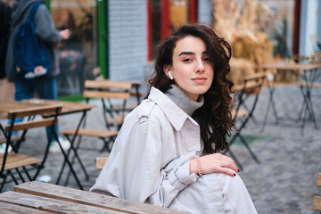 Attractive stylish brunette girl listening music in wireless earphones dreamily looking in camera on street