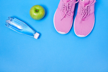 Pink sport shoes with green apple and bottle of water on a blue background. Concept healthy lifestyle, sport and diet. 