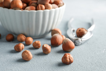 Bowl with tasty hazelnuts and cracker on color background
