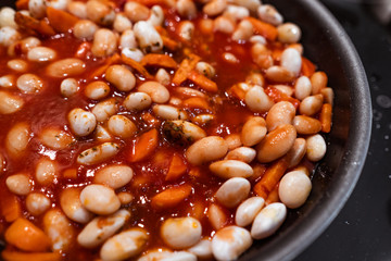 Carrots, garlic and beans with tomato sauce in a pan before cooking. Close veiw