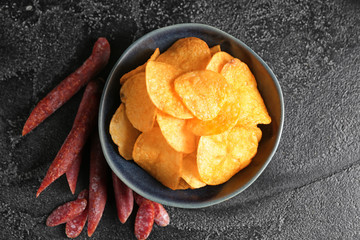 Bowl with tasty potato chips and sausages on table