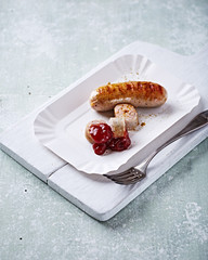 Grilled white sausage with ketchup on white paper tray. Rustic wooden background. 